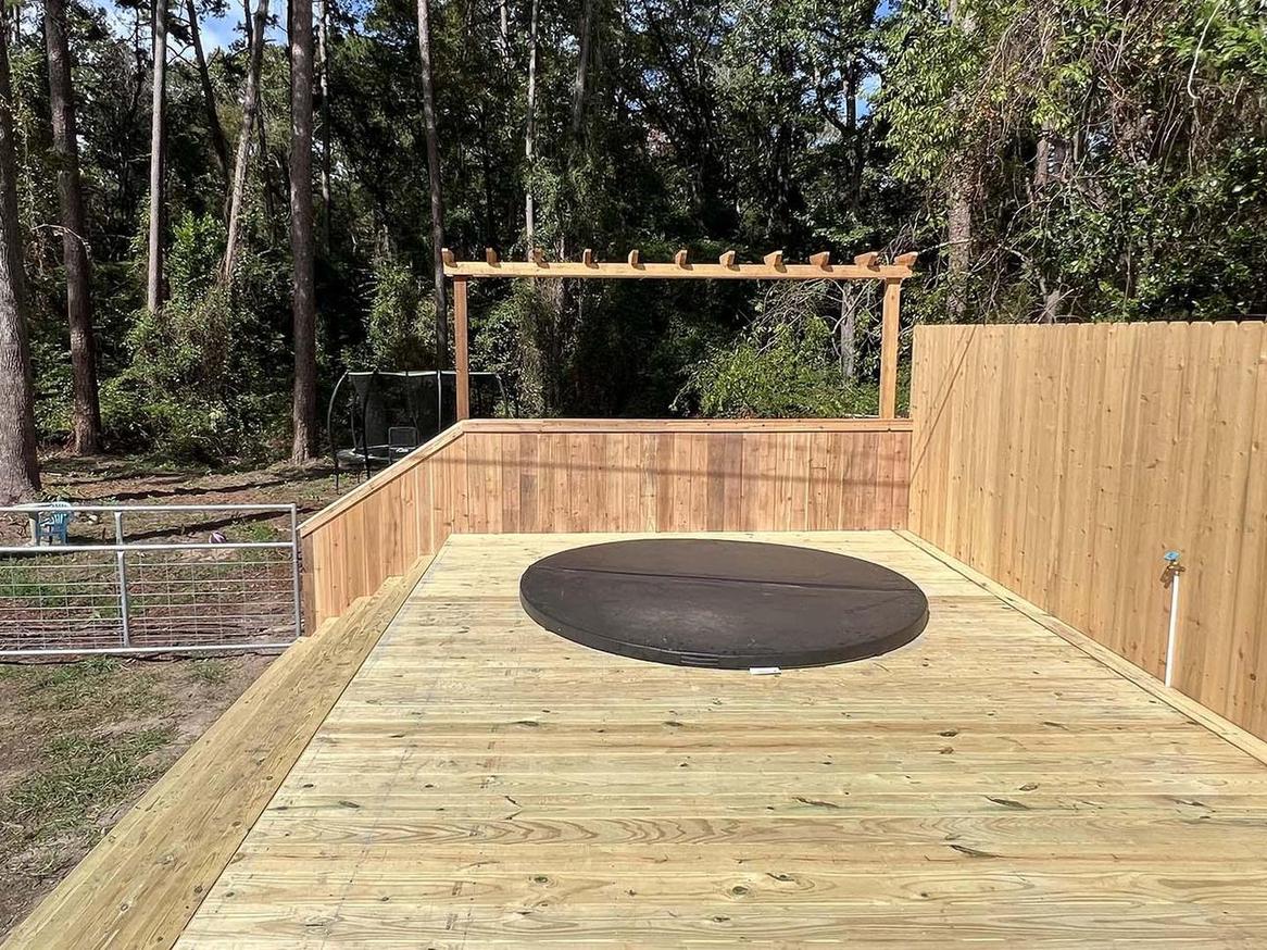 Wood deck with attached pergola and round hot tub cover overlooking a treed yard