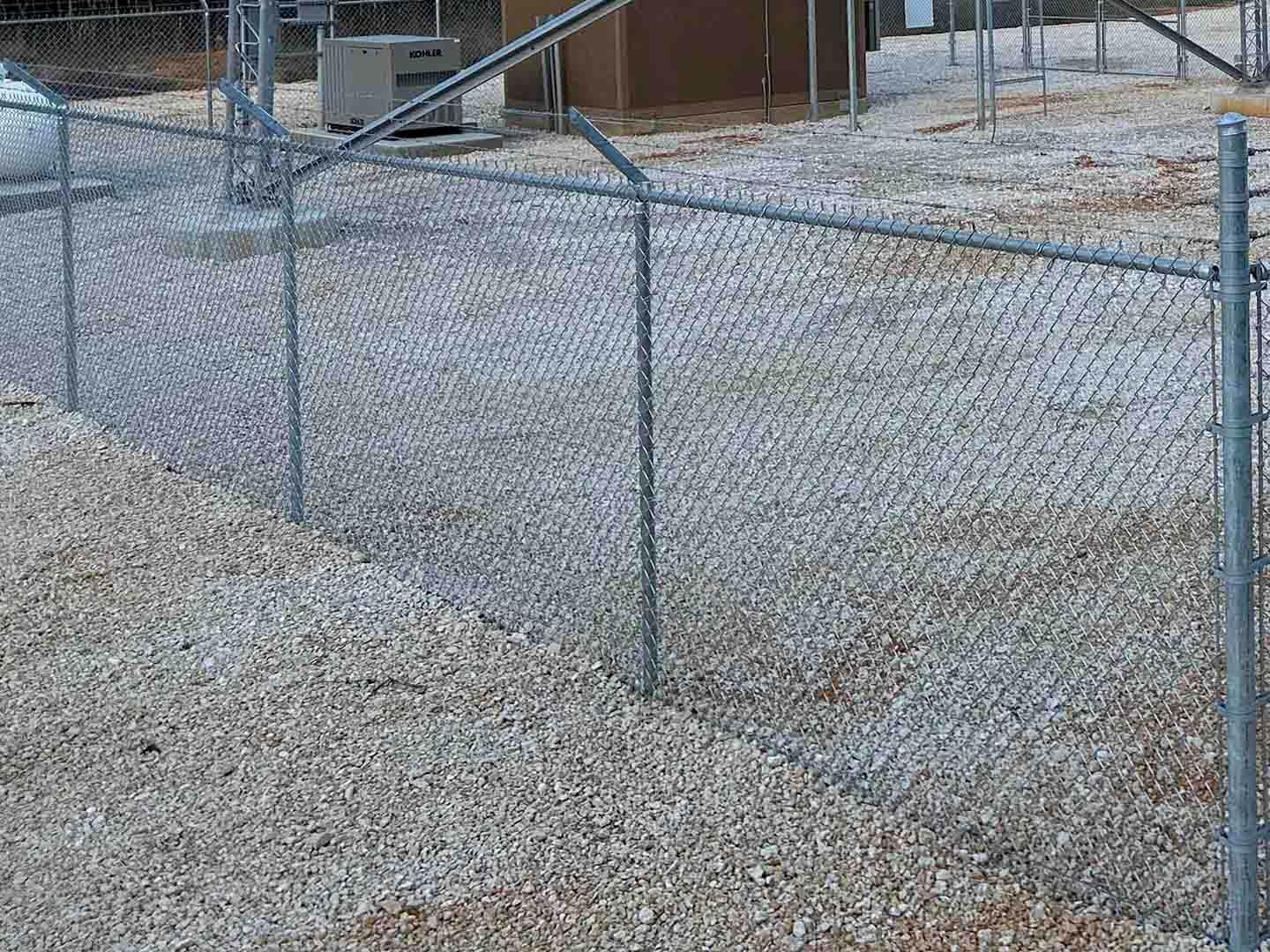 Galvanized commercial chain link fence with tension bar and top rail along a gravel yard