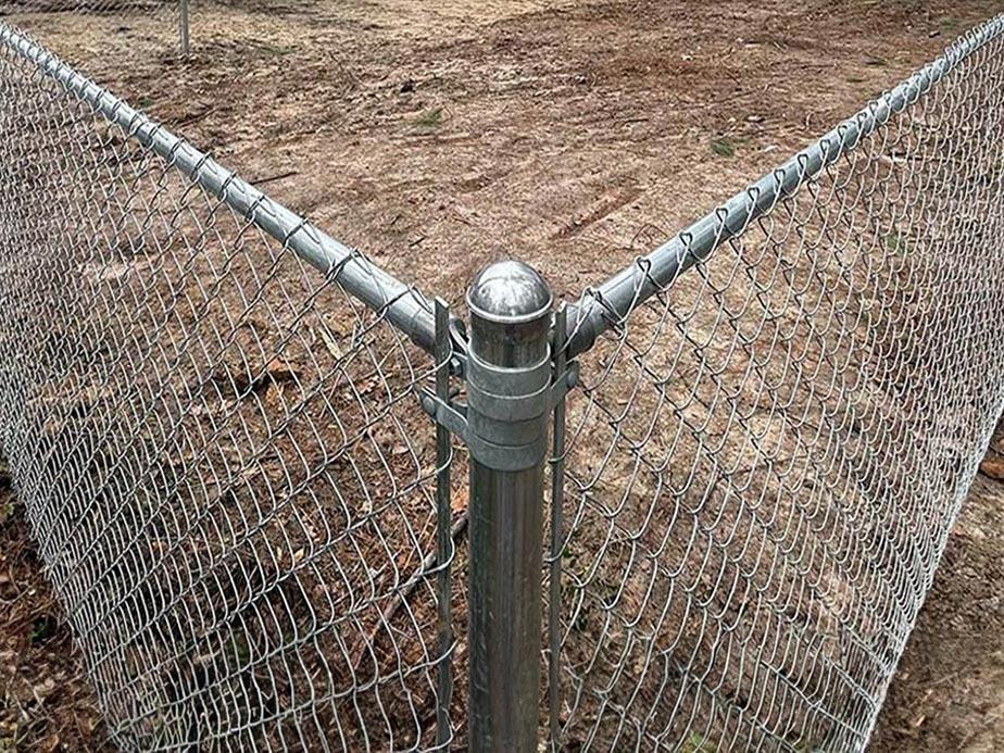 Galvanized chain link fence corner post with silver cap on bare ground