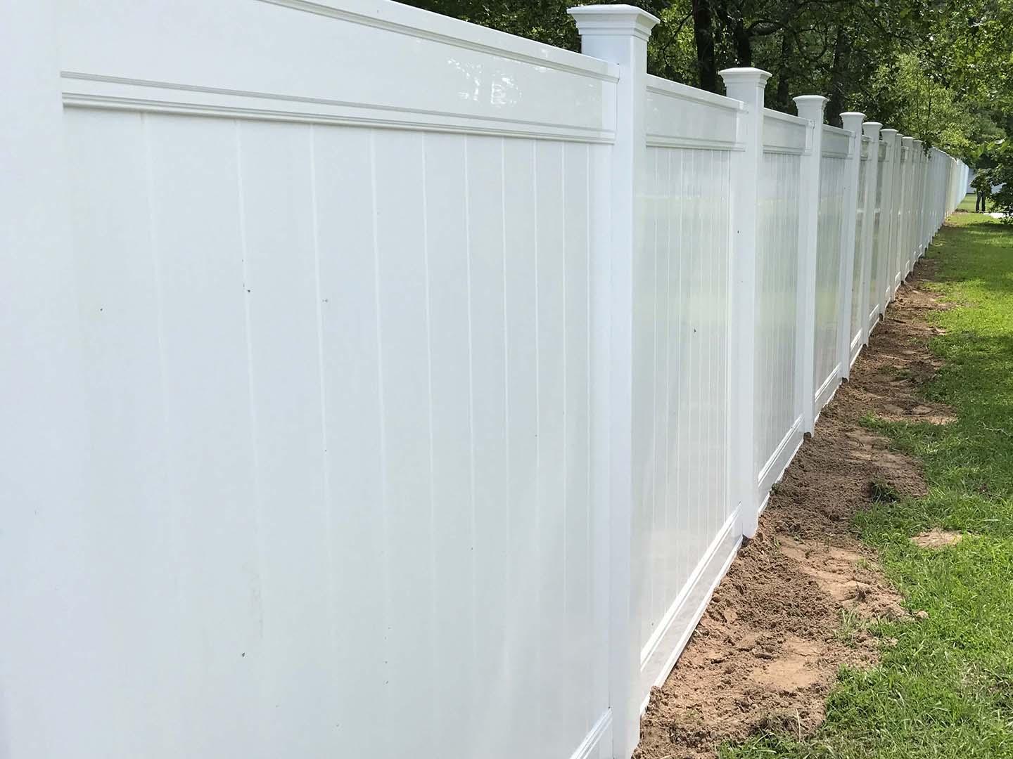 Tall white vinyl privacy fence with decorative post caps along a property line