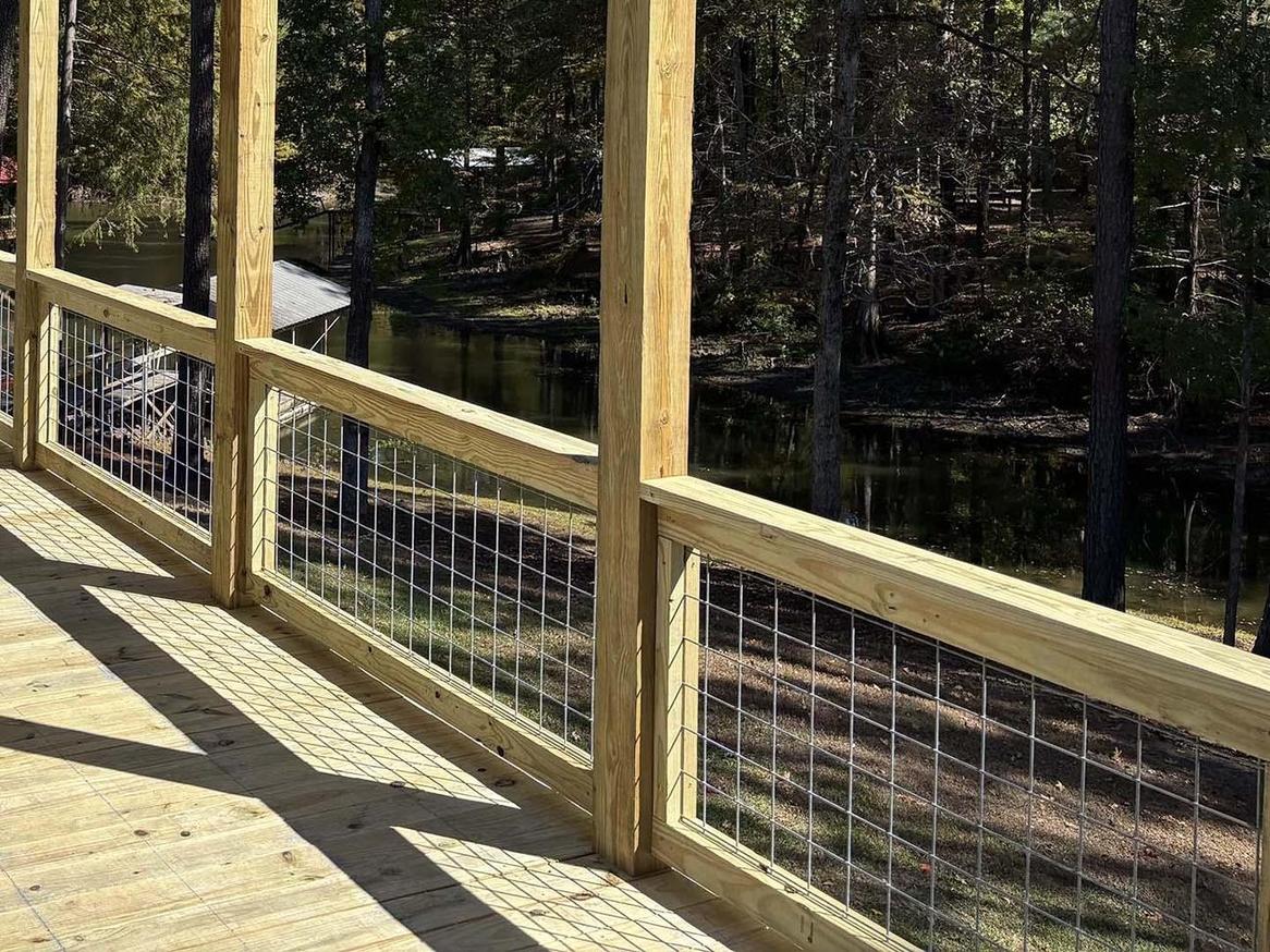 Pressure-treated wood deck railing with wire mesh panels overlooking a lake